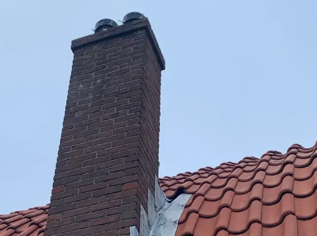 Gemetselde schoorsteen — Een hoge gemetselde schoorsteen boven een rood pannendak.