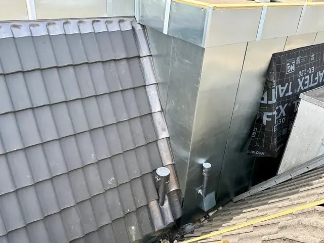 Bekleding naast dakpannen — Metalen zijbekleding bij de overgang naar een schuin pannendak.