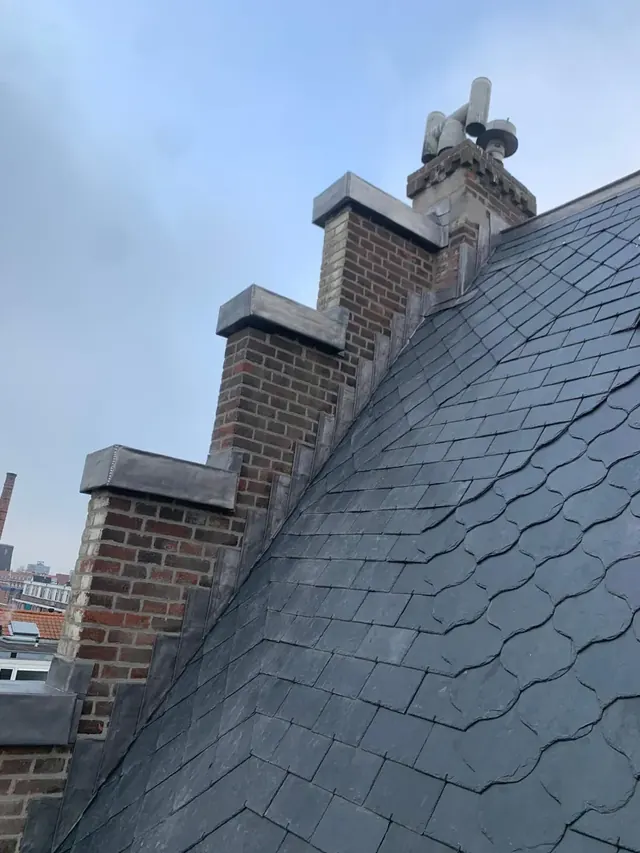 Leien langs een trapgevel — Leien dakvlak met een gemetselde trapgevel en metalen aansluitingen.